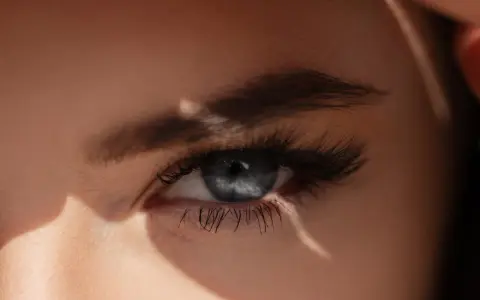 Un œil bleu intense, sublimé par un microblading parfait, capte la lumière du soleil.