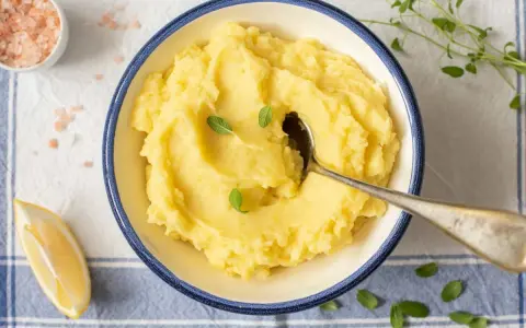 Un cremoso puré de patata de la abuela, servido en un cuenco azul, con una cuchara, limón y sal rosa.