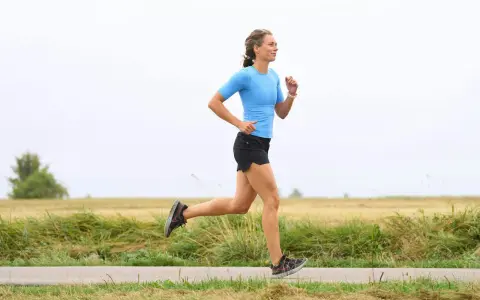 Kvinna i blå tröja och svarta shorts springer på en landsväg. Hon har en imponerande **run streak** och njuter av löprundan i det öppna landskapet.