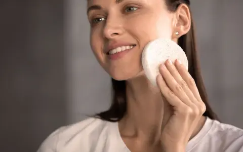 Une femme souriante utilise une éponge naturelle pour se laver le visage. Une méthode douce pour un nettoyage en douceur.