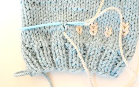 Agujas de punto plumeti dos agujas, creando un delicado diseño de hojas en tejido azul claro.