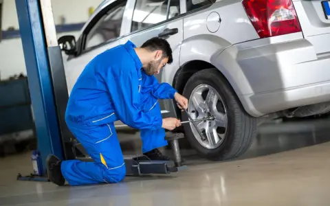 Meccanico in tuta blu lavora sulla ruota anteriore di un'auto argentata sollevata da un ponte.