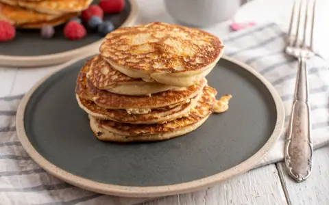 Stos puszystych fit pancakes z odżywki białkowej, ozdobiony malinami i borówkami, czeka na widelcu.