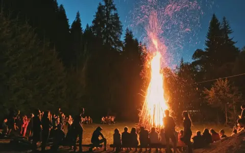 Människor samlas runt en stor brasa i skogen, en vacker svensk tradition som lyser upp natten med gnistor och värme.