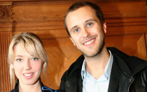 Oskar Linnros och Veronica Maggio ler mot kameran, med en träbakgrund som ger en varm känsla.