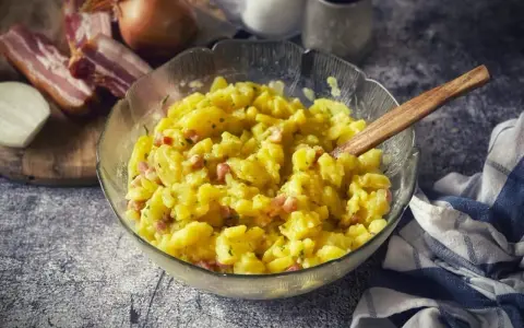 Ein Schüssel voller warmer Kartoffelsalat mit Speck und Zwiebeln, bereit zum Servieren.