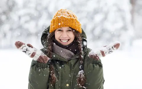 Una chica sonríe felizmente en medio de una nevada, con su gorro naranja y guantes a juego. ¡Bonitas fotos en la nieve!