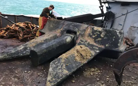Un marin prépare une énorme ancre de bateau, expliquant comment fonctionne une ancre de bateau : elle s'enfonce dans le fond marin pour stabiliser le navire.
