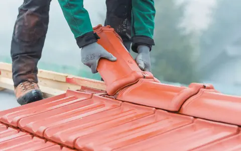 Dachówka ceramiczna w rękach dekarza. Czy remont dachu wymaga pozwolenia na budowę? Zależy od zakresu prac.