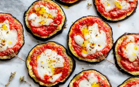 Deliziose pizzette di melanzane con pomodoro e mozzarella filante, condite con olio e erbe aromatiche.