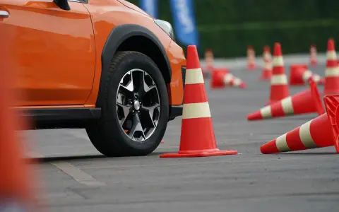 Pomarańczowy samochód na placu manewrowym, otoczony pachołkami. Może to być przygotowanie do obowiązkowej wymiany prawa jazdy.