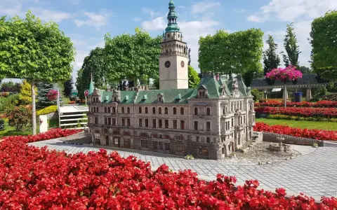 Miniatura ratusza z wieżą zegarową, otoczona czerwonymi kwiatami. Jedna z wielu atrakcji Kotliny Kłodzkiej.