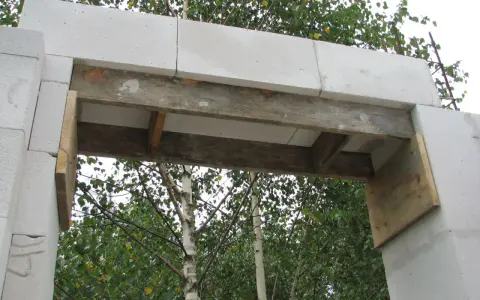 Zbrojenie nadproża 3m z bloczków betonowych, podparte drewnianymi belkami, gotowe do dalszych prac budowlanych.