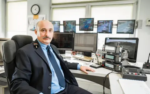 Mężczyzna w mundurze siedzi przy biurku z wieloma monitorami pokazującymi trasy kolejowe i urządzenia komunikacyjne.