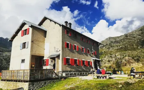 Rifugi raggiungibili in auto a Bergamo: un edificio con persiane rosse in montagna, con persone sedute fuori.