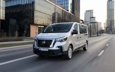 Srebrny van Nissan, jeden z najnowszych nissan modele, jedzie ulicą w nowoczesnym mieście.
