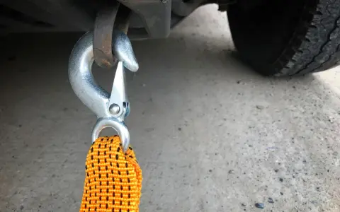 Gancio metallico agganciato al telaio di un'auto, pronto per iniziare a come trainare una macchina. La cinghia arancione è visibile.