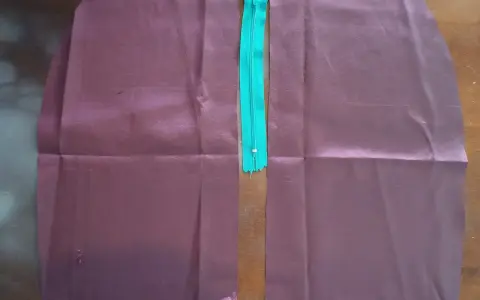 Dwa kawałki bordowego materiału przygotowane do wszywania zamka. Zamek jest turkusowy i leży pośrodku.