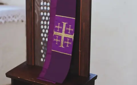 Fioletowa stuła z krzyżami, symbol przygotowania do spowiedzi wielkanocnej, wisi na drewnianej kratce konfesjonału.