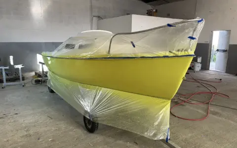 Un bateau jaune est bâché pour le repeindre. Il est sur une remorque dans un atelier.