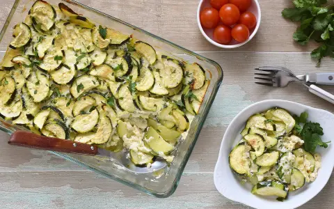 Delicioso calabacín al horno, gratinado y espolvoreado con perejil fresco. Servido en una fuente de vidrio y un plato blanco.