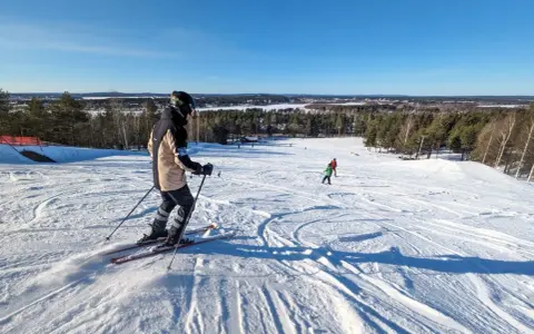Person åker skidor i Luleå en solig dag. Barn åker skidor i bakgrunden.