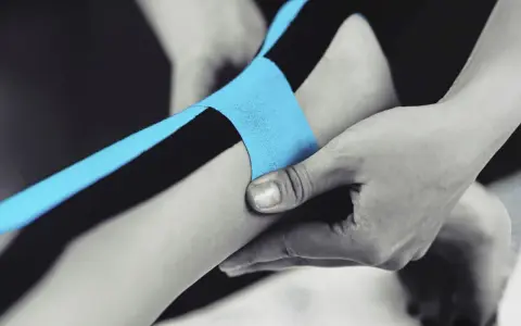 Applicazione di nastro kinesiologico blu e nero per supportare il tendine d'Achille.