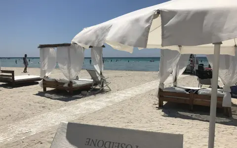 Beach cabanas with white curtains and beds on a sandy beach with the ocean in the background.