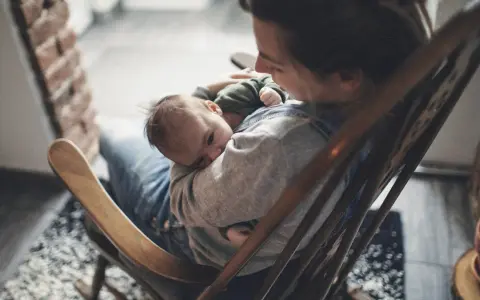 Ein Baby schläft friedlich auf dem Arm einer Person, die in einem Schaukelstuhl sitzt. Es ist, als ob die Babys im Bauch noch träumen, bevor sie die Welt entdecken.