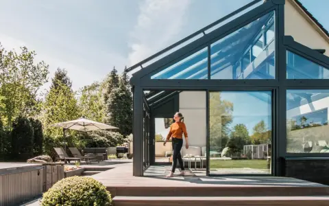 Frau betritt modernen Wintergarten mit Glasdach. Perfekt, um den Sommer zu verlängern und den **Wintergarten planen**.