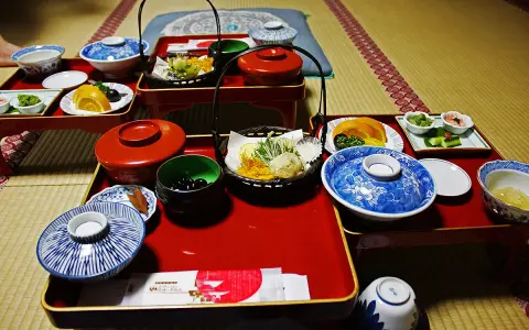A traditional Japanese meal, perhaps a monk diet, featuring small dishes of tempura, fruit, pickles, and black beans on red lacquer trays.