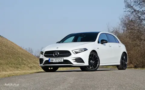 Biały Mercedes A250 z czarnym dachem i felgami stoi na drodze, na tle wzgórza i drzew.