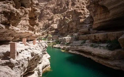Wadi Shab w Oman: czy warto? Zielona woda w kanionie, skalne ściany i ścieżka z kamiennymi słupkami. Niesamowite widoki.