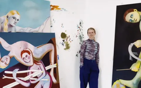 A woman stands in her studio surrounded by her surreal, figurative paintings, showcasing her as one of today's popular contemporary artists.