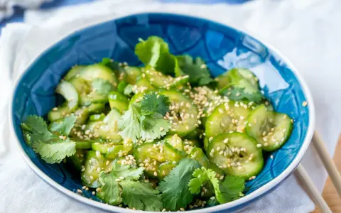 Frischer Gurkensalat mit Sojasauce, Koriander und Sesam in einer blauen Schüssel.
