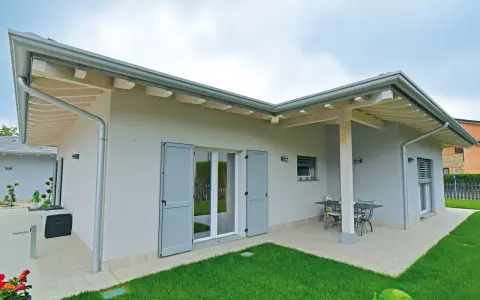Esterni di case moderne ad un piano con tetto spiovente, ampie vetrate e un patio con tavolo.