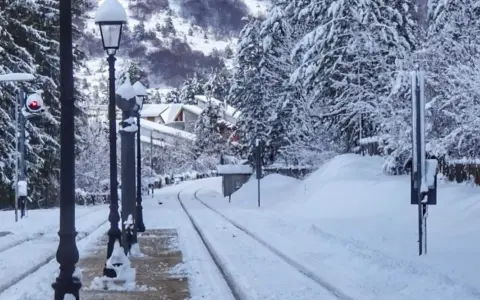 Stazione innevata, binari coperti di neve, lampioni e alberi imbiancati. Un paesaggio da **campo di Giove** in inverno.