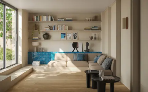 Un salón moderno con suelo de madera clara y paredes en tonos neutros. Un sofá beige se complementa con cojines azules. La pared del fondo presenta un detalle de azulejos azules vibrantes, creando un contraste llamativo y logrando un perfecto combinar ...