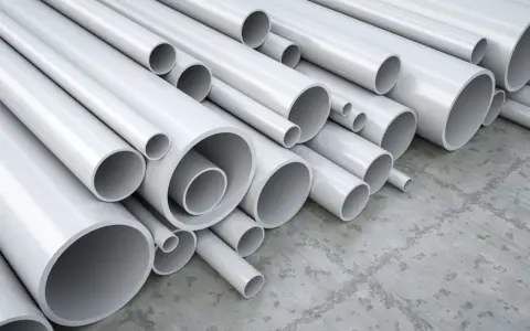 A pile of white pipes, many of which are made of vinyl, a type of plastic, are stacked on a concrete floor.