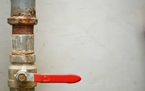 Tubería oxidada con una llave de paso general roja, lista para controlar el flujo.