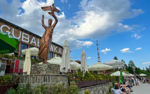 Gubałówka atrakcje: pomnik z orłem, restauracje, parasole i ludzie odpoczywający na ławkach.
