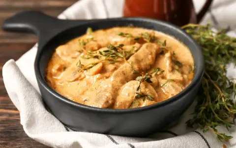 Cremiges Rindfleisch mit Pilzen, garniert mit frischem Thymian. Ein köstliches stroganoff rezept original, serviert in einer schwarzen Schüssel.