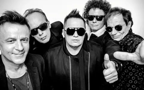 Pięciu mężczyzn w okularach przeciwsłonecznych, gotowych na koncert. Jeden z nich pokazuje kciuk w górę, jakby mówił "t.love hau! hau!".