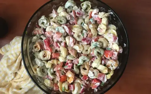 Kolorowa sałatka z tortellini, papryką i majonezem w szklanej misce.