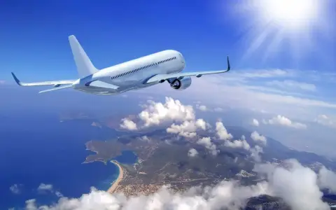 Un aereo bianco solca il cielo azzurro sopra una costa frastagliata. Il sole splende, creando un senso di distacco del vitreo e aereo.