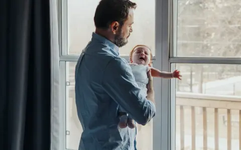 Ojciec trzyma płaczące dziecko przy oknie, gdy matka wychodzi.