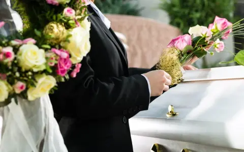 Białe i różowe róże, często wybierane jako kwiaty na pogrzebie starszej osoby, zdobią trumnę.