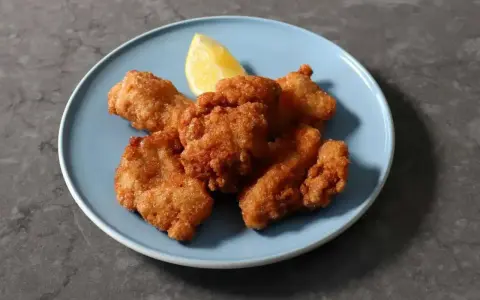 Chrupiący kurczak karaage na niebieskim talerzu, z kawałkiem cytryny.