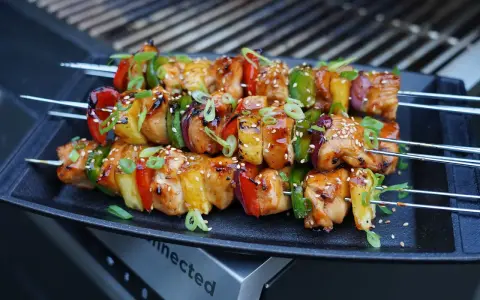 Huli Huli Chicken Spieße mit Paprika, Zwiebeln und Ananas, glasiert und mit Sesam bestreut, auf einem Grill.