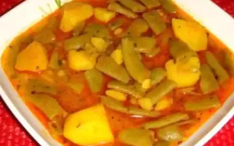 Un plato humeante de judías verdes con patatas, cocinado en una sabrosa salsa rojiza.